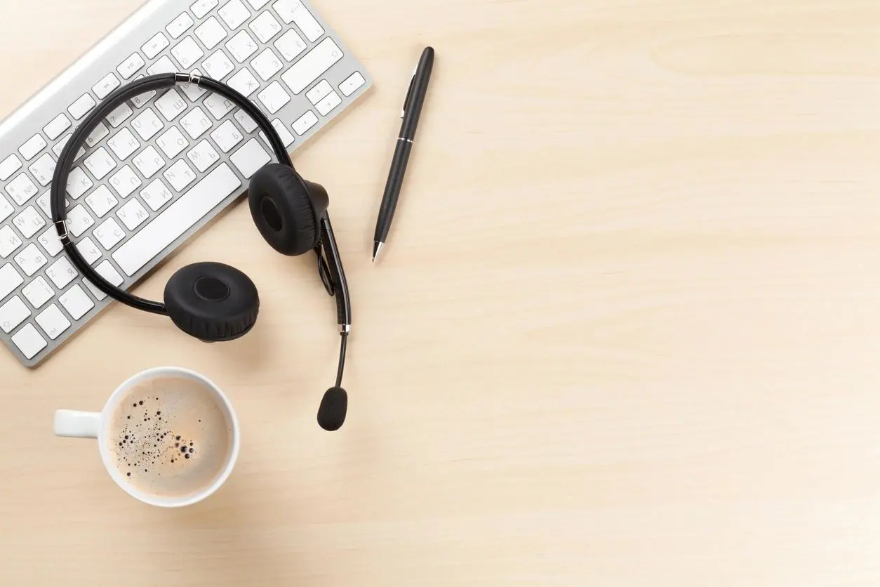A desk with headphones, keyboard and coffee cup.